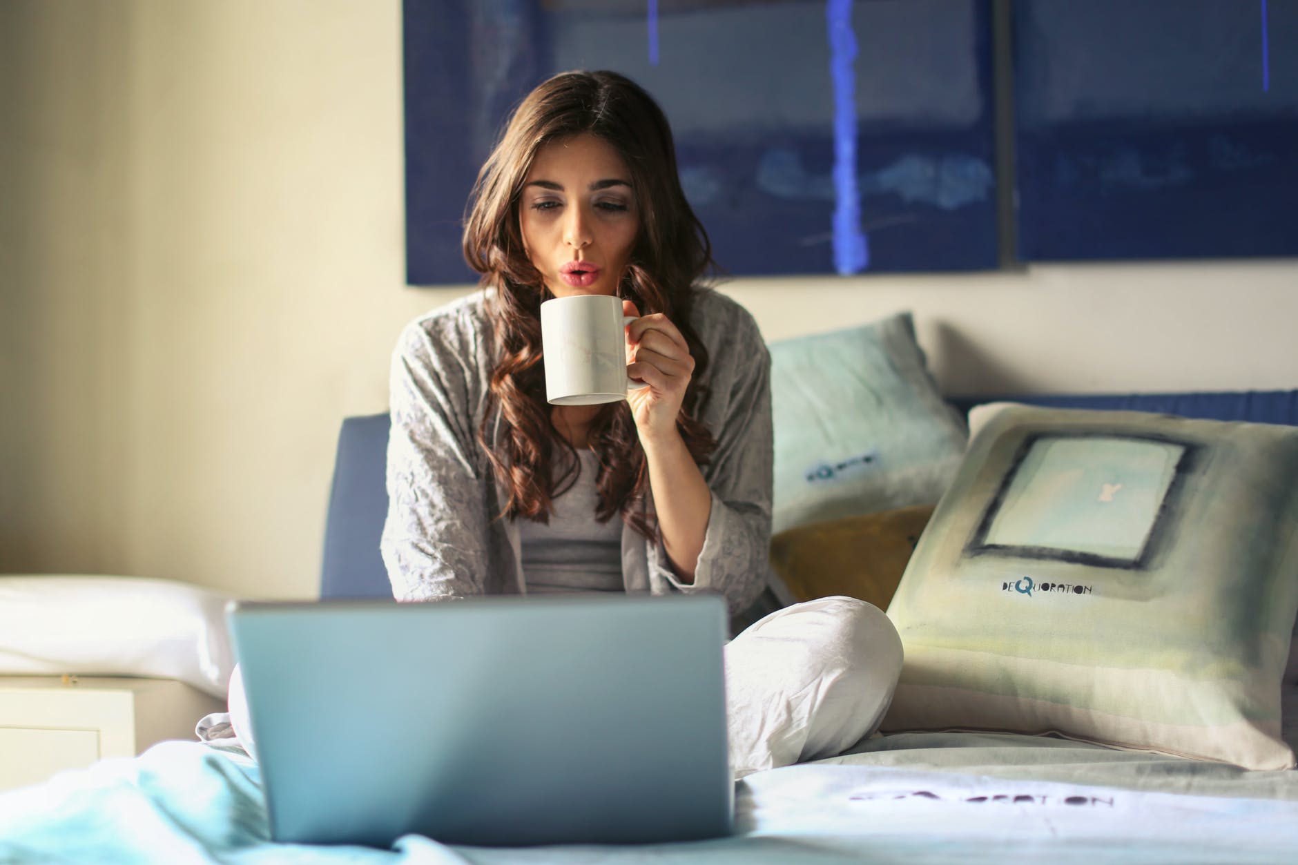 woman in grey jacket sits on bed uses grey laptop to switch CRM